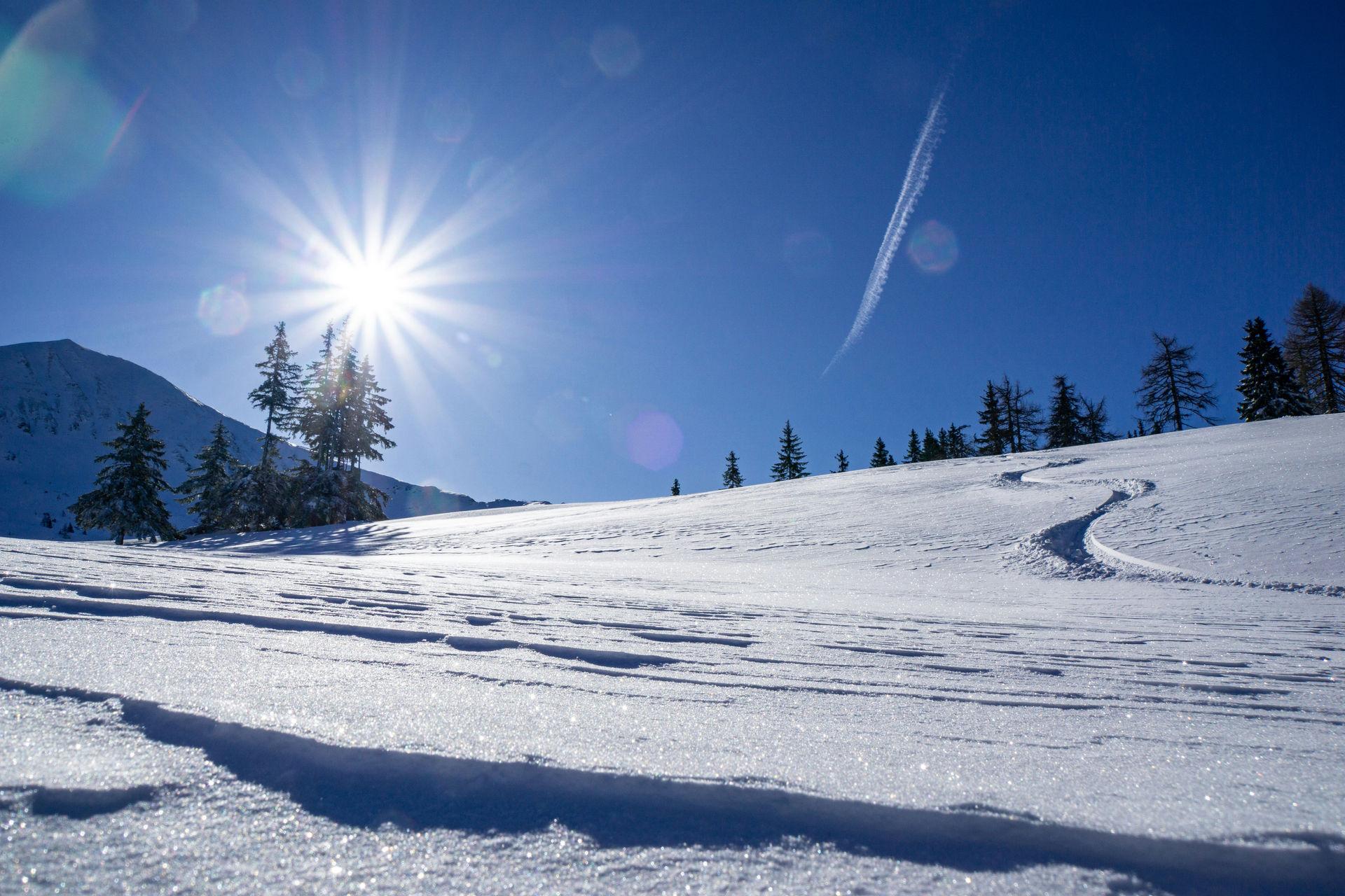 Verschneiter Hang mit Loipenspur und Bergen im Allgäuer Winter.