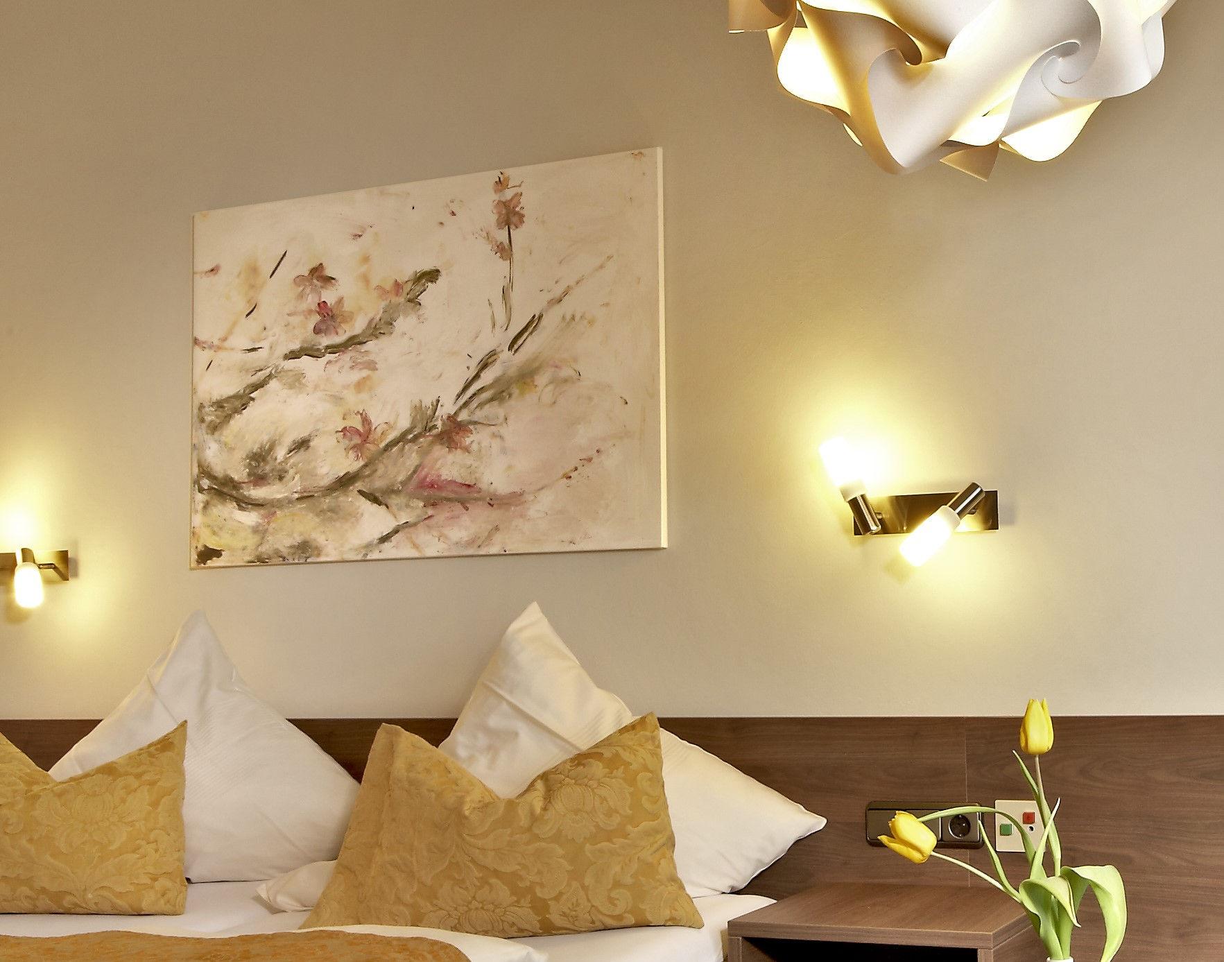 Gemütliches Hotelzimmer mit Bett, Kunstwerk, modernen Lampen und gelben Tulpen.