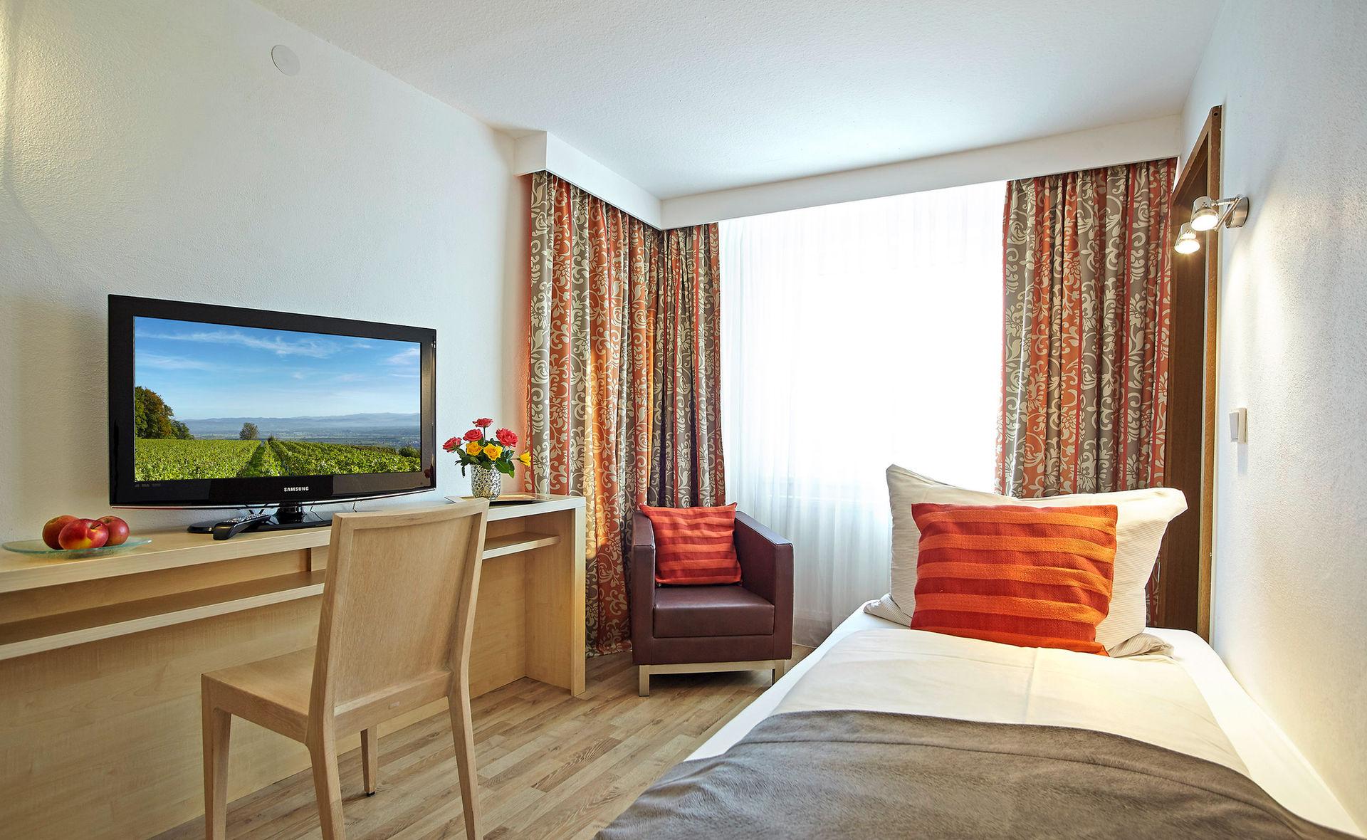 Helles Hotelzimmer EINZELZIMMER mit Einzelbett, Schreibtisch, Fernseher und Sessel.