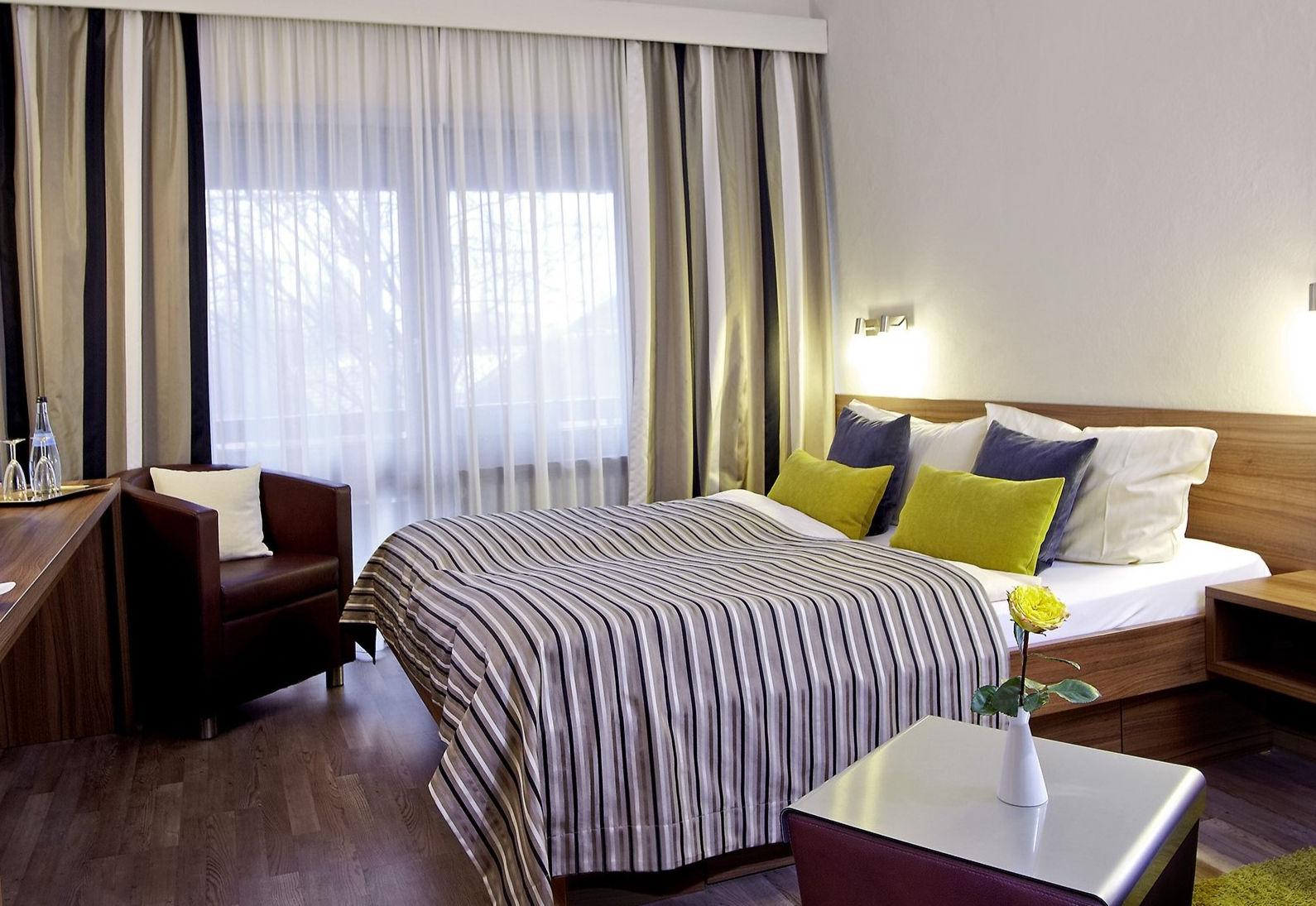 Modernes Hotelzimmer mit Doppelbett, gestreifter Bettwäsche, Sessel und Fenster