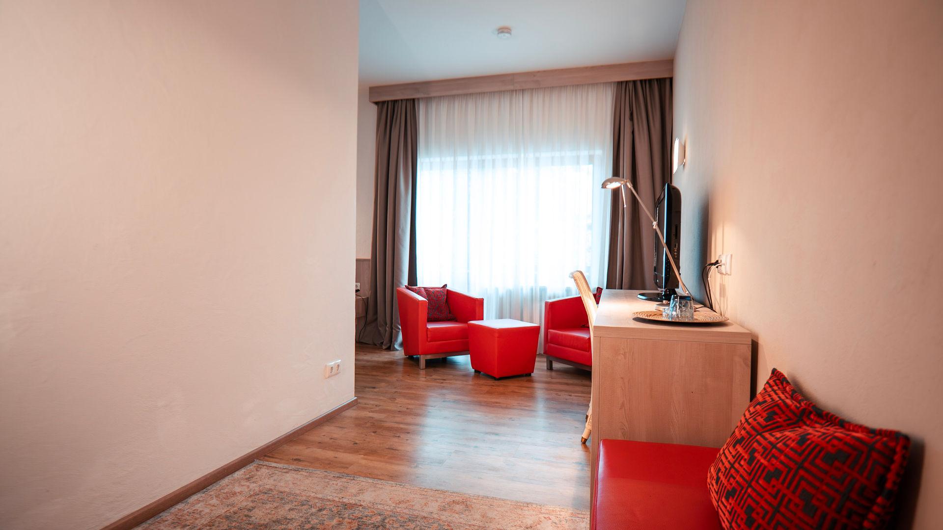 Modernes Hotelzimmer mit rotem Sessel, Tisch, Schreibtisch und Fenster.