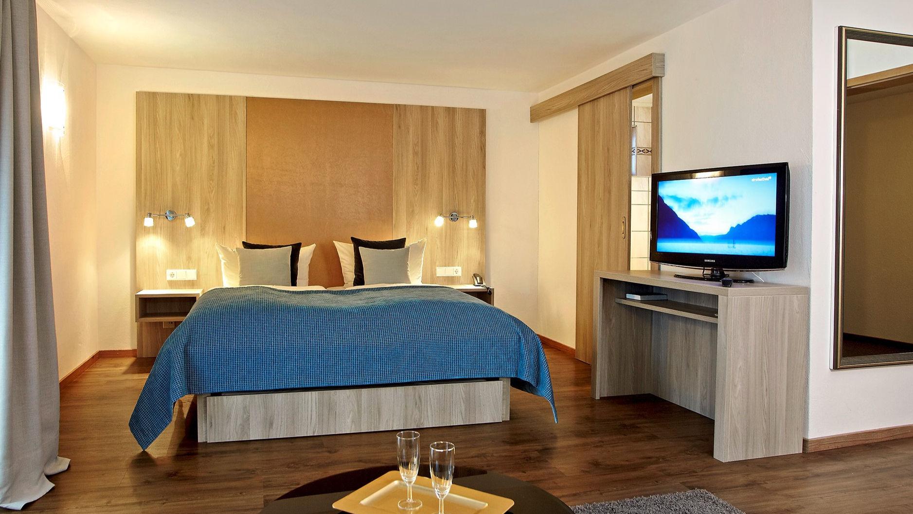 Modernes Hotelzimmer mit großem Bett, Holzdekor und Fernseher für Gäste.