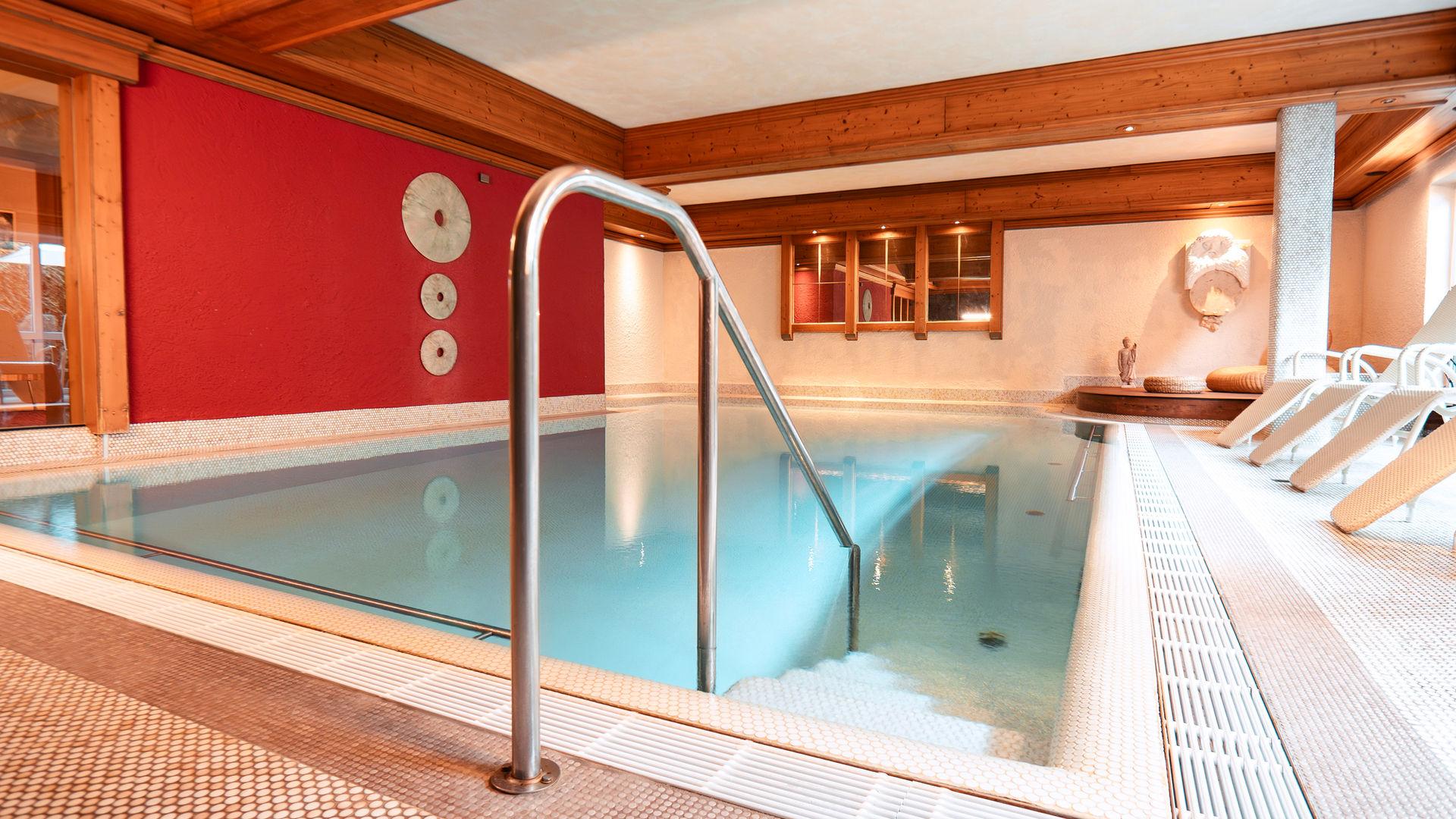 Hallenbad mit türkisem Wasser, roter Wand und Holzdecke.