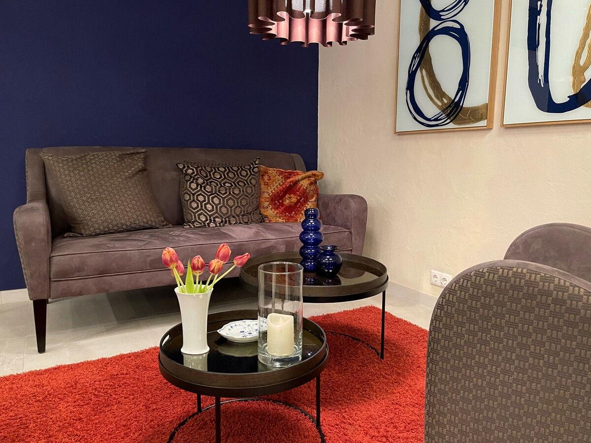 Loungebereich mit Sofa, rotem Teppich und Tulpen auf dem Beistelltisch.