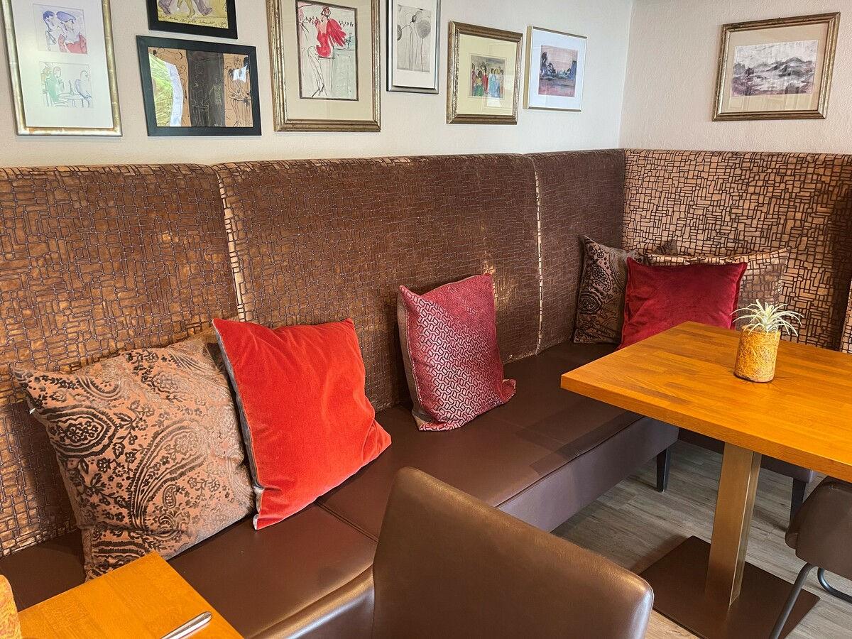 Restaurantnische mit gepolsterter Sitzbank, Kissen und Bildergalerie.