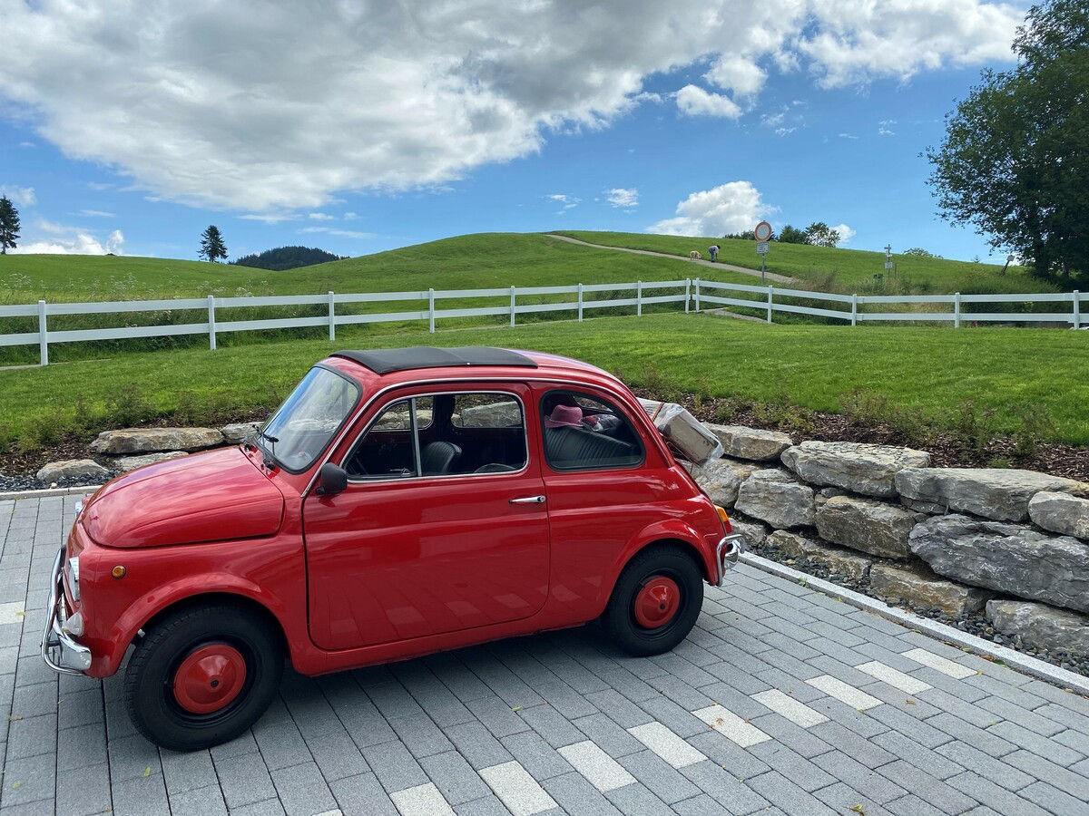 Roter Fiat 500 Oldtimer auf der gepflasterten Hoteleinfahrt vor grünen Hügeln.