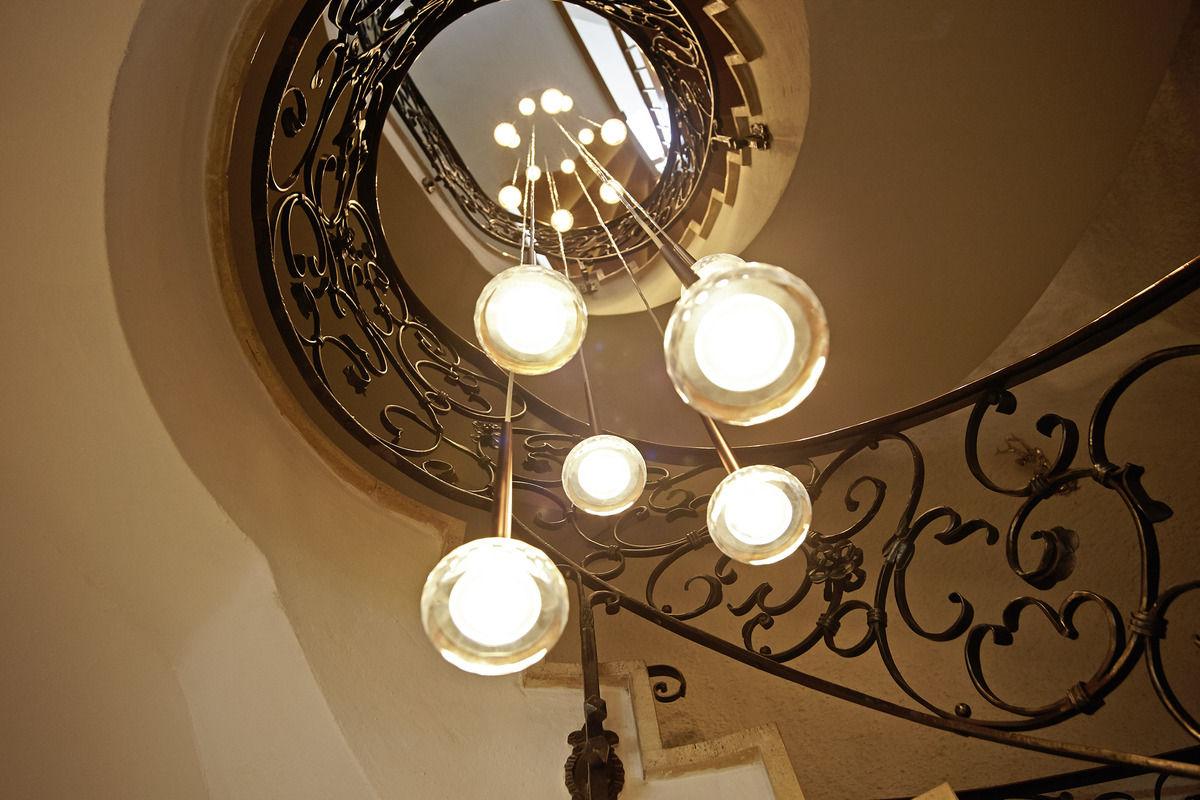 Treppenhaus mit geschwungenem Schmiedeeisengeländer und moderner Kugelleuchte.