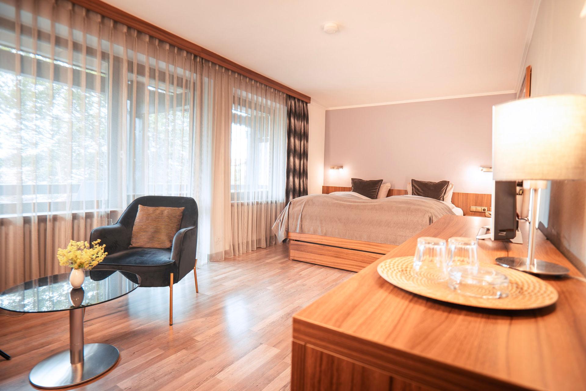 Modernes Hotelzimmer mit Doppelbett, Sessel, Holzboden und großen Fenstern.